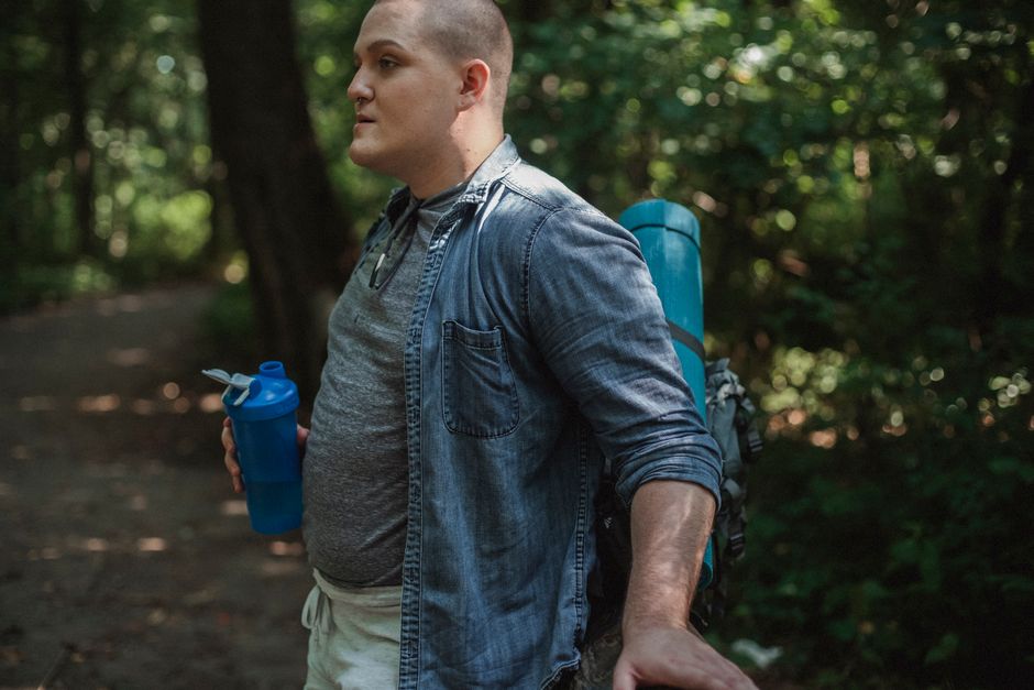 Side view of serious traveler with backpack standing with bottle of water in hand and resting in forest in daytime