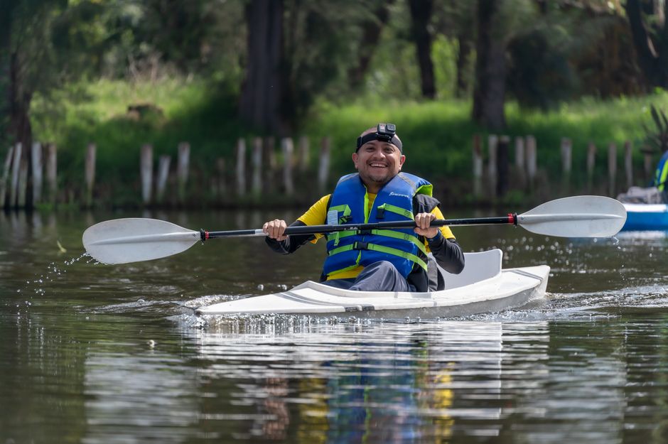 Smiling man kayaking with a paddle and life jacket in Xochimilco, Mexico.
